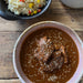 A styled overhead shot of a meal on a rustic wooden table, featuring a bowl of mole sauce with meat and a side of rice with vegetables. The word 'Mole.