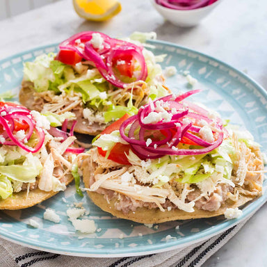 Tostadas with chicken, lettuce, tomatoes, and pickled onions on a blue plate.